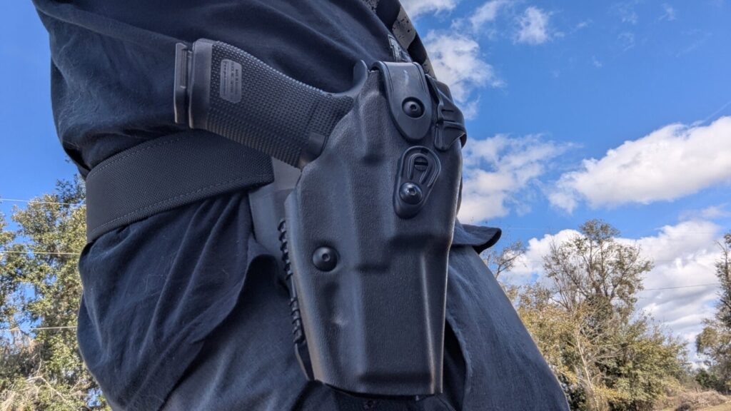 Side view of a Safariland 6360RDS holster containing a Glock pistol, worn on a duty belt by a person in a black shirt.