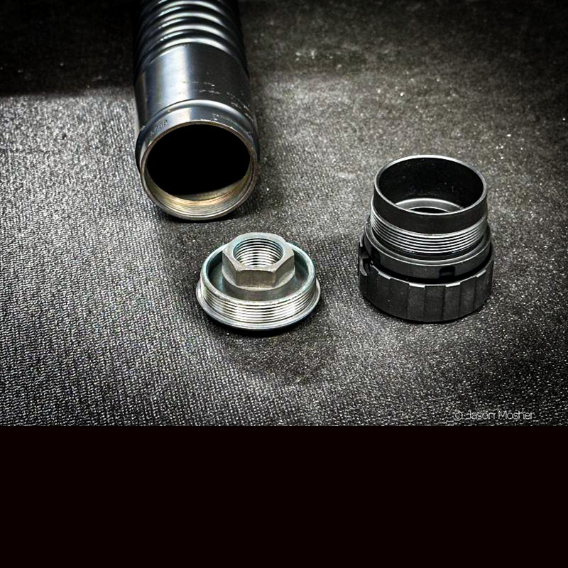 A black A-10 silencer with the mount removed from the back. It is on a table with two mounts laying next to it. 