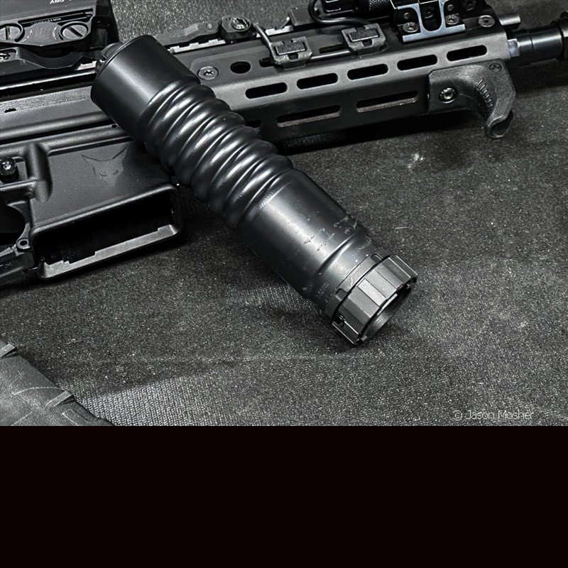 A black A-10 silencer leaning on a rifle, on a black table. 