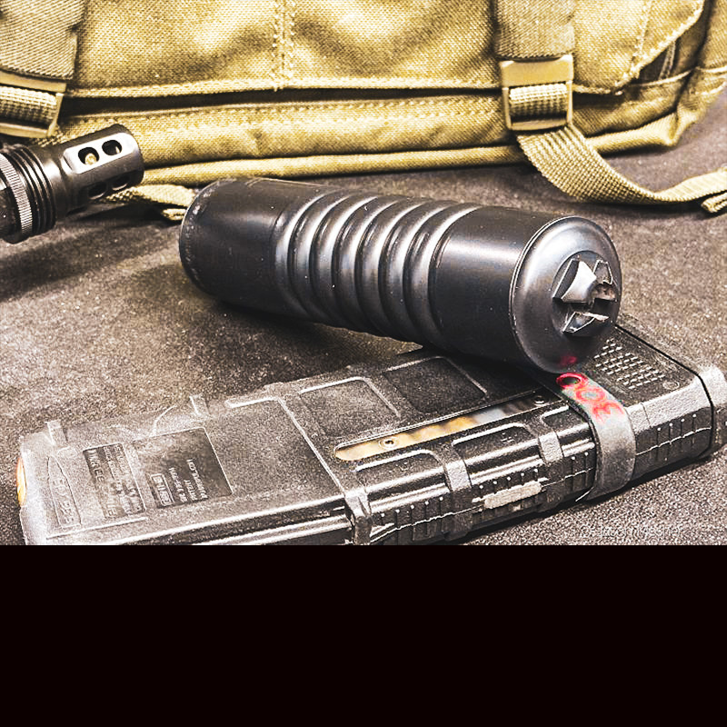 A black silencer laying on an AR-15 magazine with a green bag in the back ground. 