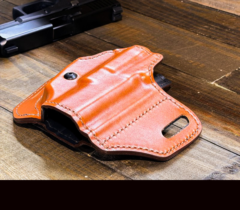 A brown leather holster laying on a wood table.