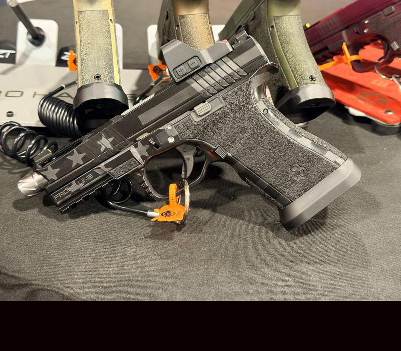 A black gun with a silver barrel leaning up against some other guns during a gun show.