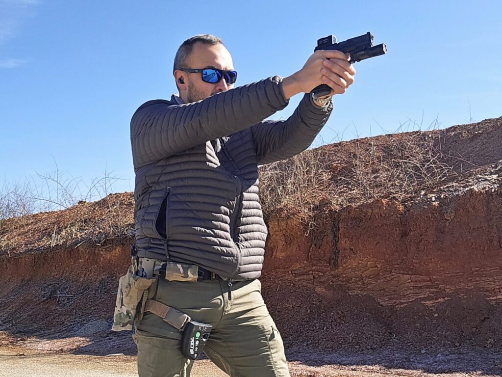 A man in a gray jacket holding a pistol at a shooting range