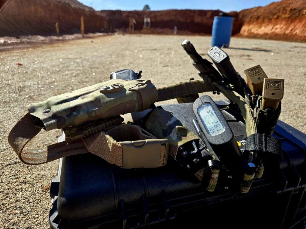 A pistol belt on top of a pelican case with a shot timer at a range