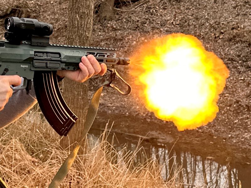 A person firing a green rifle with a bright yellow fire-ball coming out of the end of the barrel. 