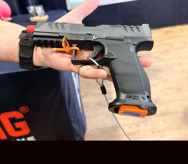 A person holding a Walther PDP black pistol in their hand with an orange training magazine in it. 