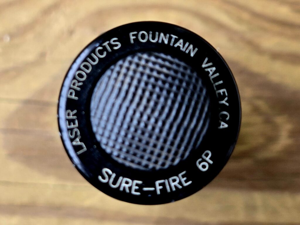 A flashlight tail cap against a wood backdrop