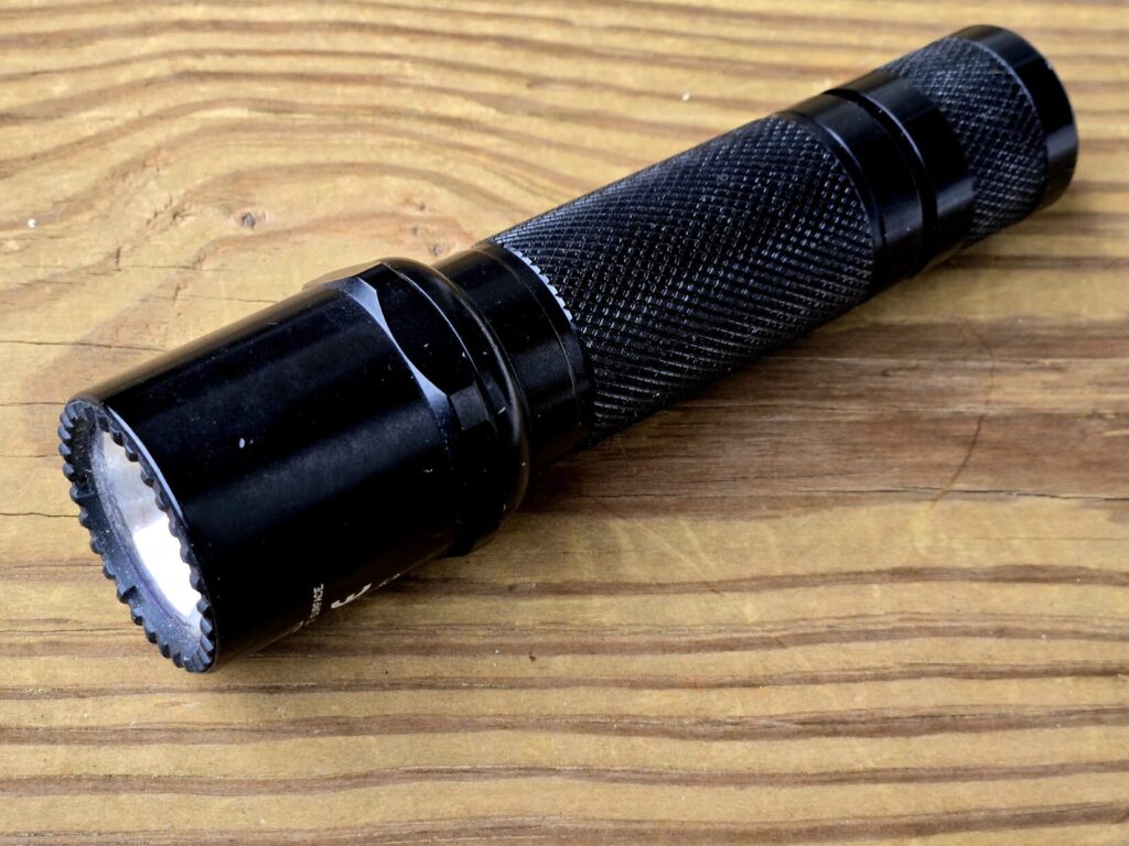 A handheld flashlight against a wood backdrop