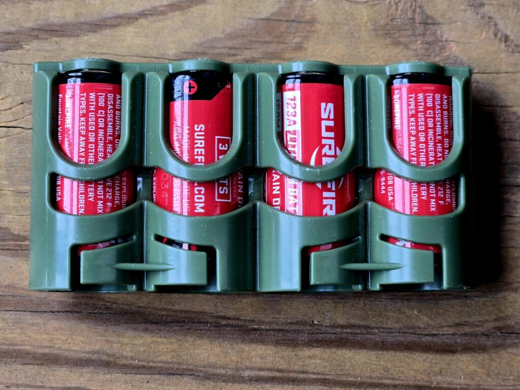 Four batteries in a plastic carrier against a wooden backdrop.