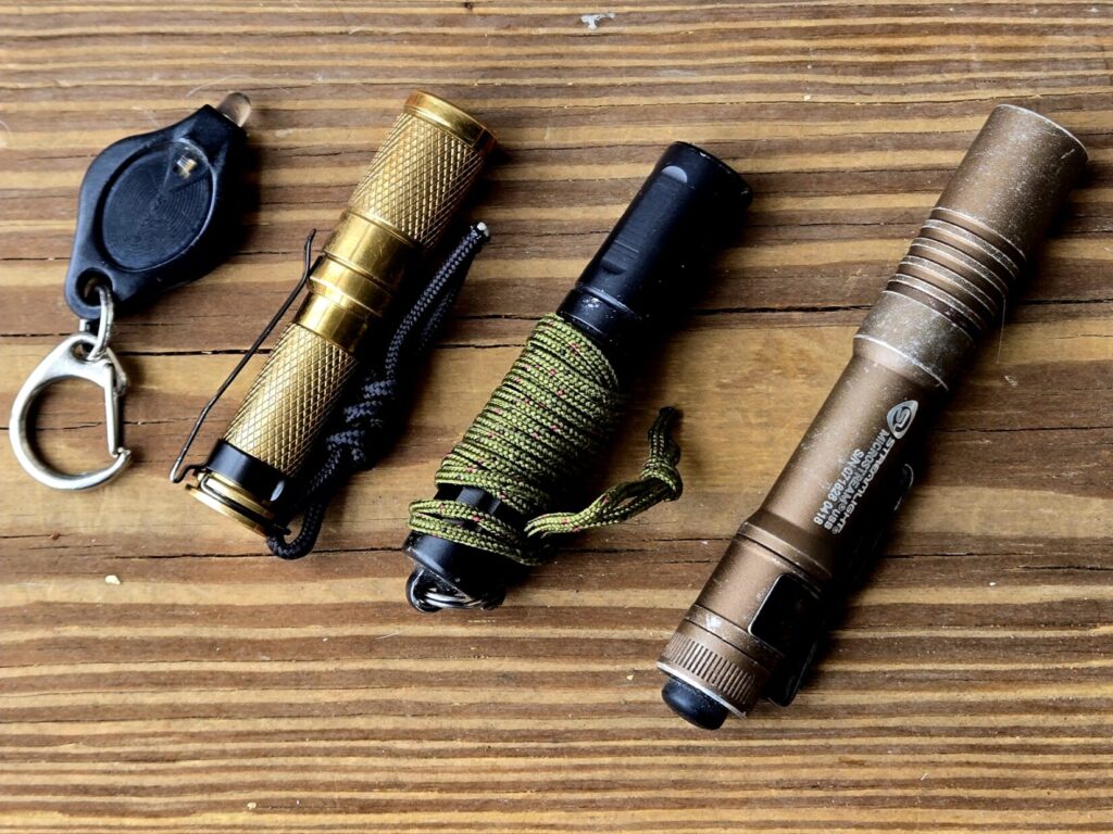 Four different small flashlights against a wooden backdrop.