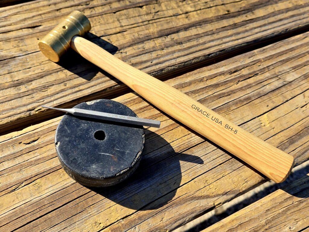 A hockey puck, brass hammer, and punch on a wooden bench