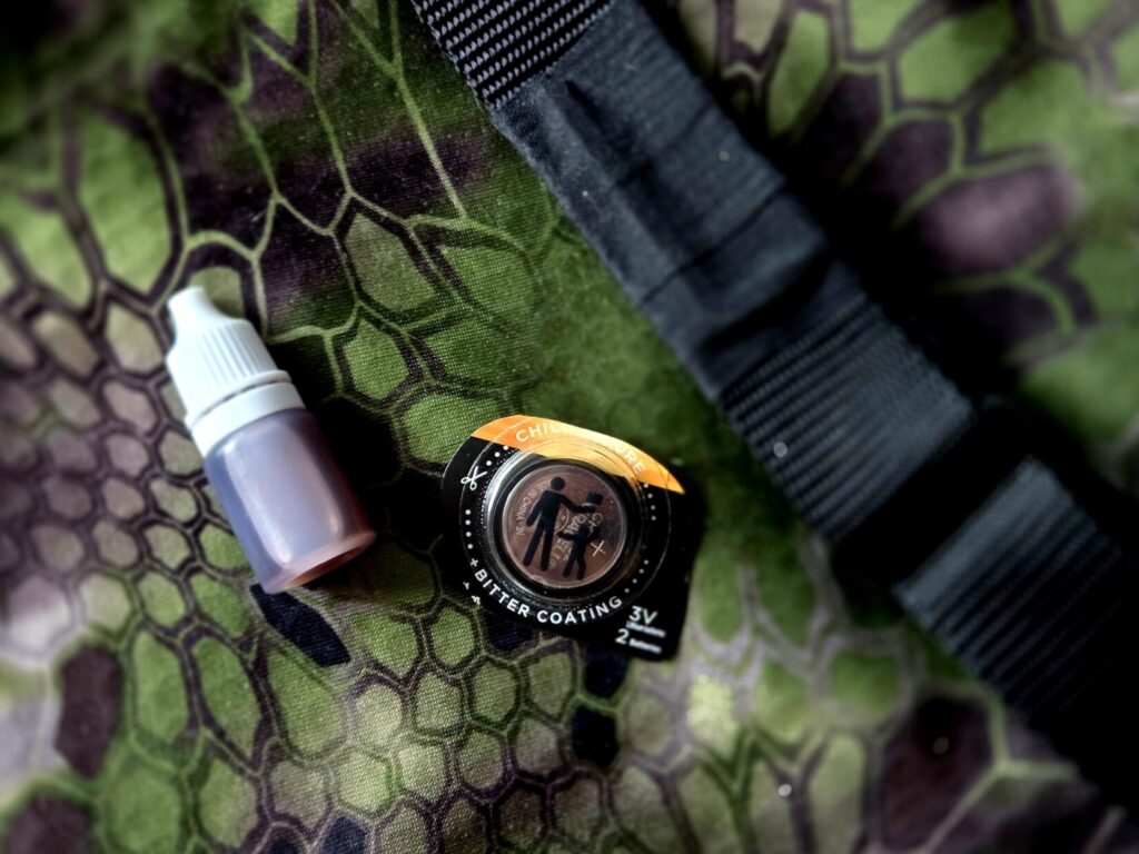 A small bottle, battery, and rifle sling against a camouflage backdrop