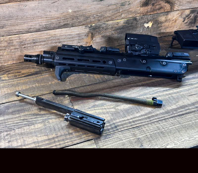 A black JAKL rifle with parts laying in front of it, after it has been field stripped. 