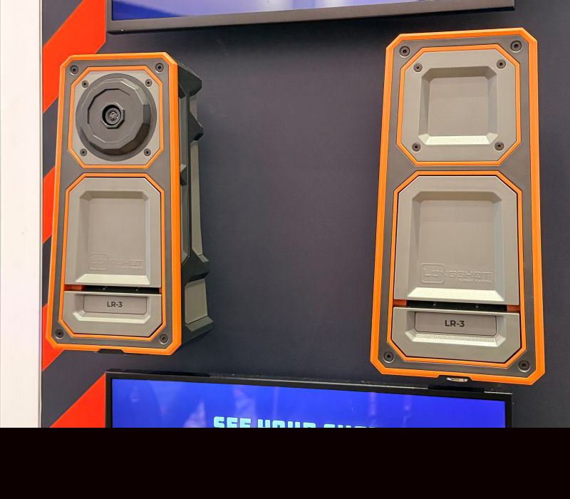 Two brown and grey cases on a wall for display. One has a camera built into the top and the other looks more like a speaker. 