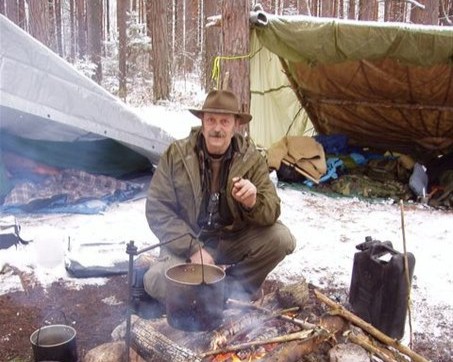 A man near a winter campfire with tarp shelters in the background