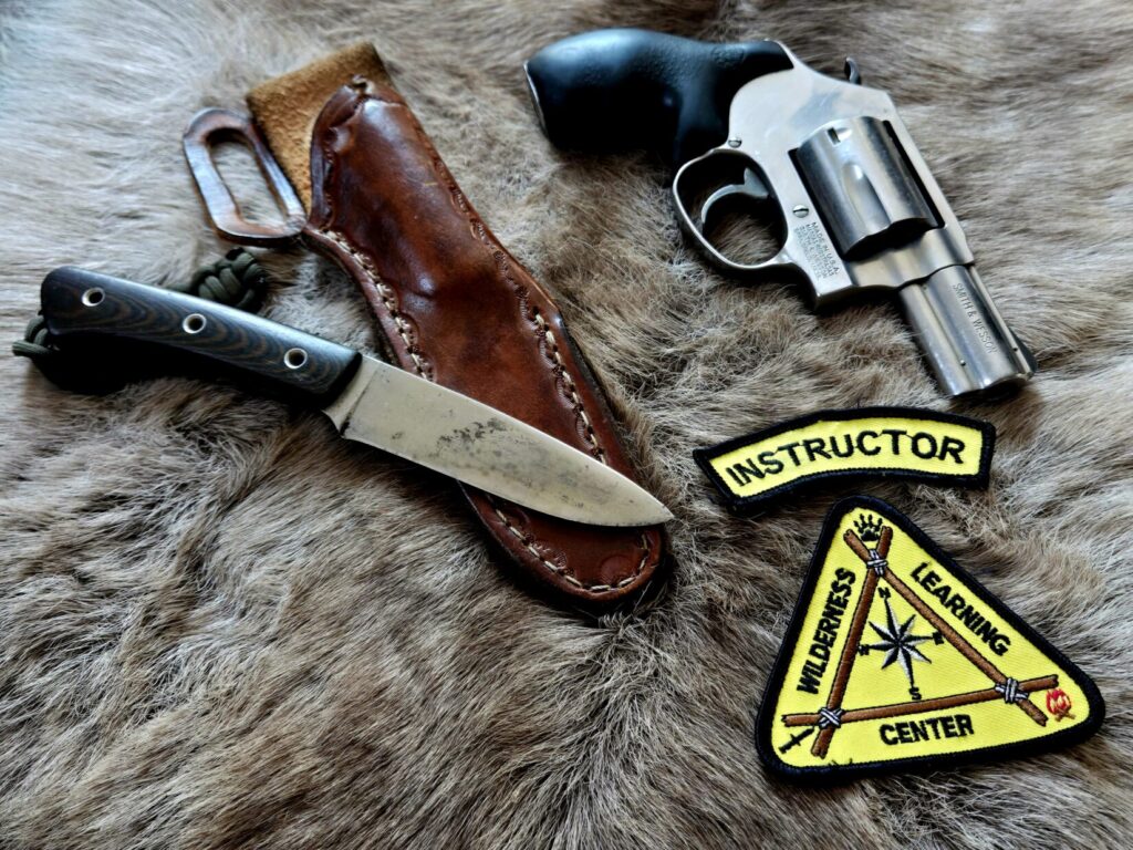 A knife and revolver on top of an animal hide with a patch