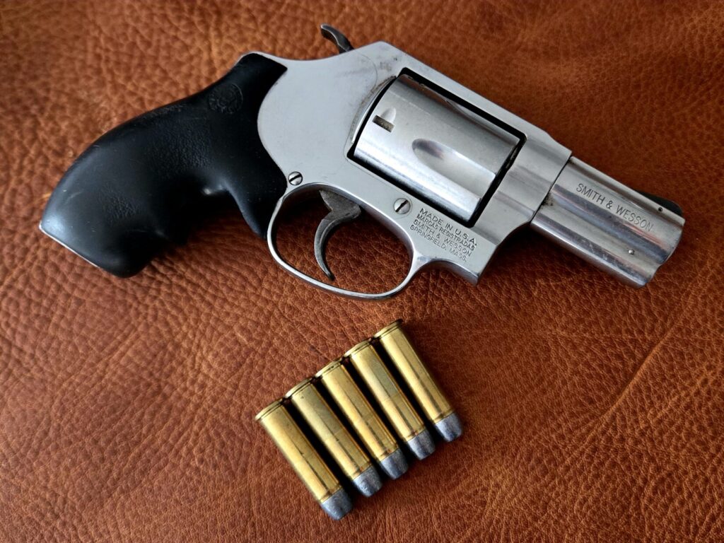 A snub nose revolver on top of a leather background with five rounds of ammo
