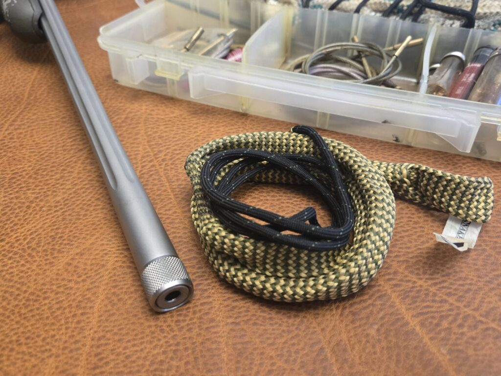 A rifle muzzle with a bore snake and miscellaneous cleaning supplies on a leather background
