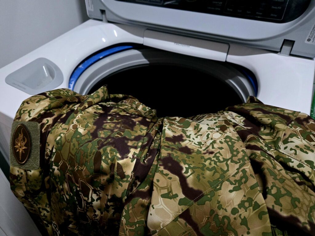 Camouflage clothing next to an open washing machine.