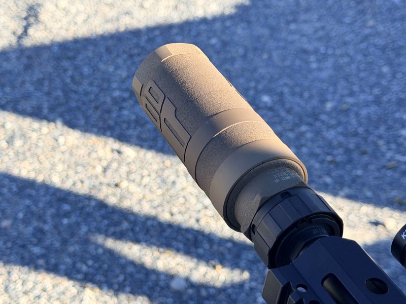 A brown silencer on the end of a black rifle. 