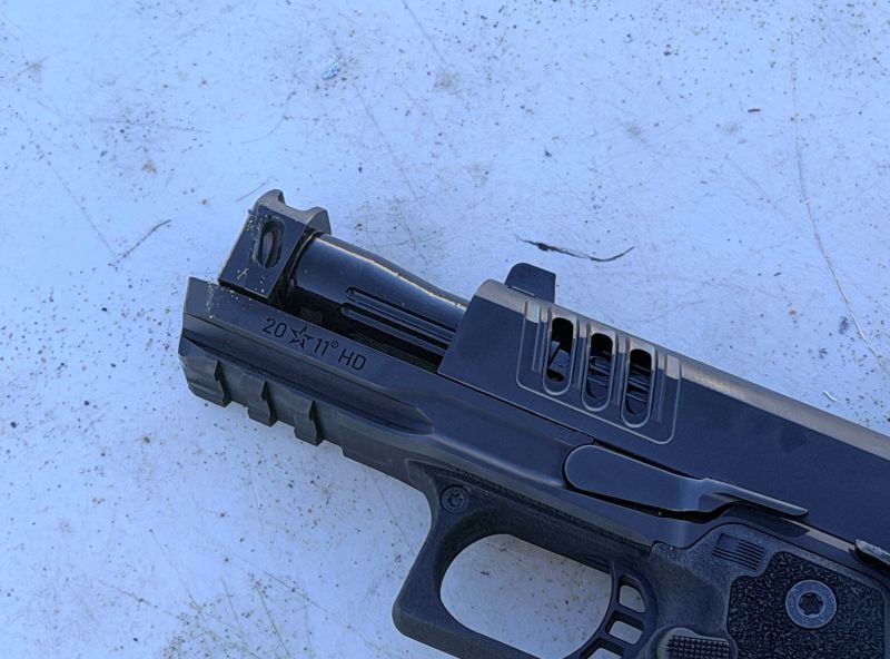 The barrel of a black handgun, showing the compensated portion. 