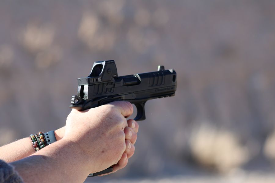 A close up of a persons hands holding a black handgun as they fire on a range. 