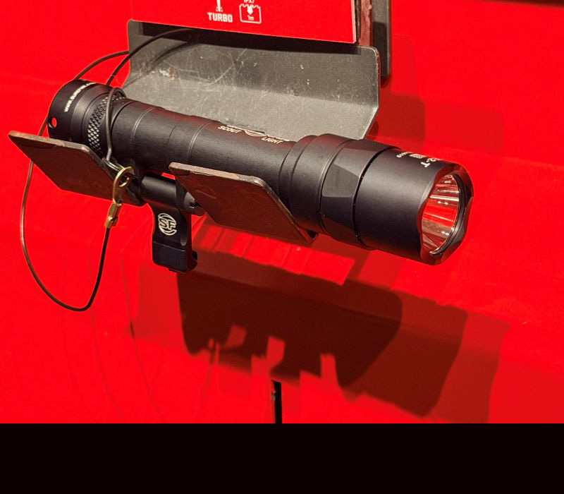 A black rifle mounted light on a stand with a red background.