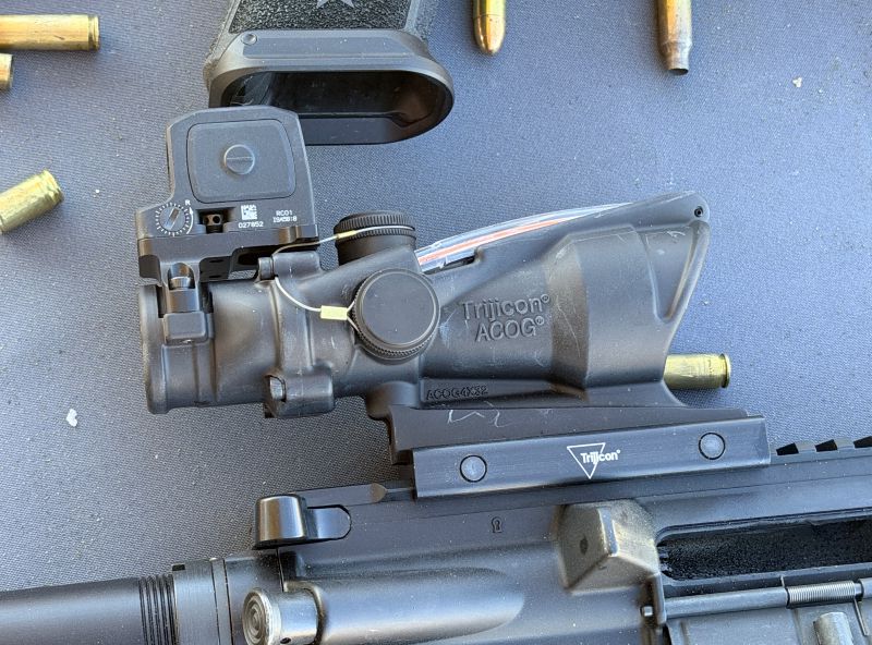 A black optic, attached to a rifle, laying on a black table. 