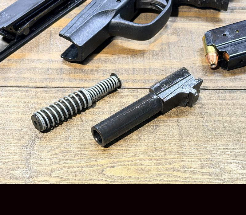 Parts from a Walther PPS M2 laying on a wood table next to the slide and grip the handgun.