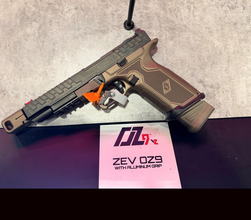 A handgun that with a greenish slide and golden color grip, leaning on a prop during a gun show.