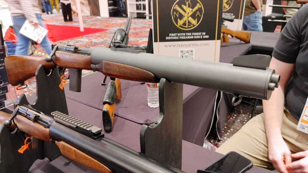 A bolt-action De Lisle carbine with an integrated suppressor and wooden stock displayed at a trade show.