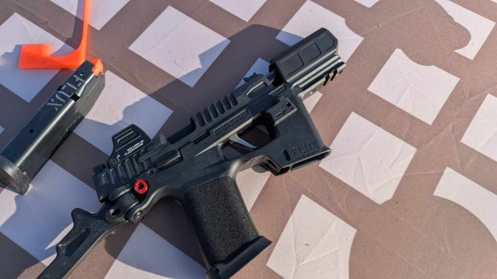 A top-down view of a Flux Defense Raider chassis with a Holosun optic and a spare magazine resting on a patterned shooting mat.