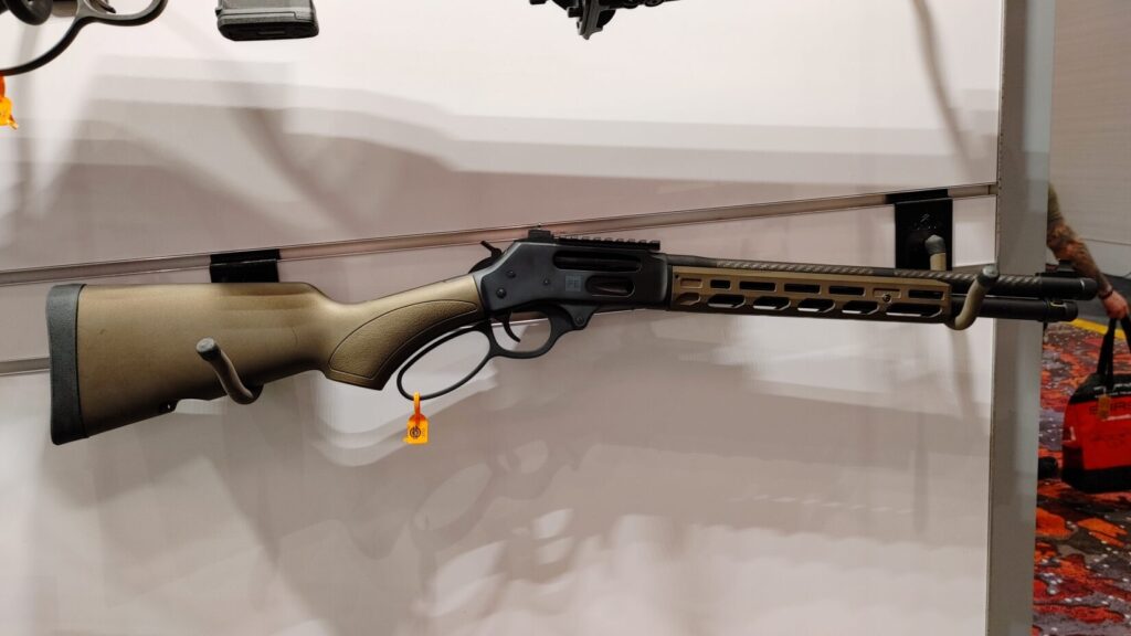 A modern lever-action rifle with an olive drab stock and an M-LOK handguard mounted on a display wall.