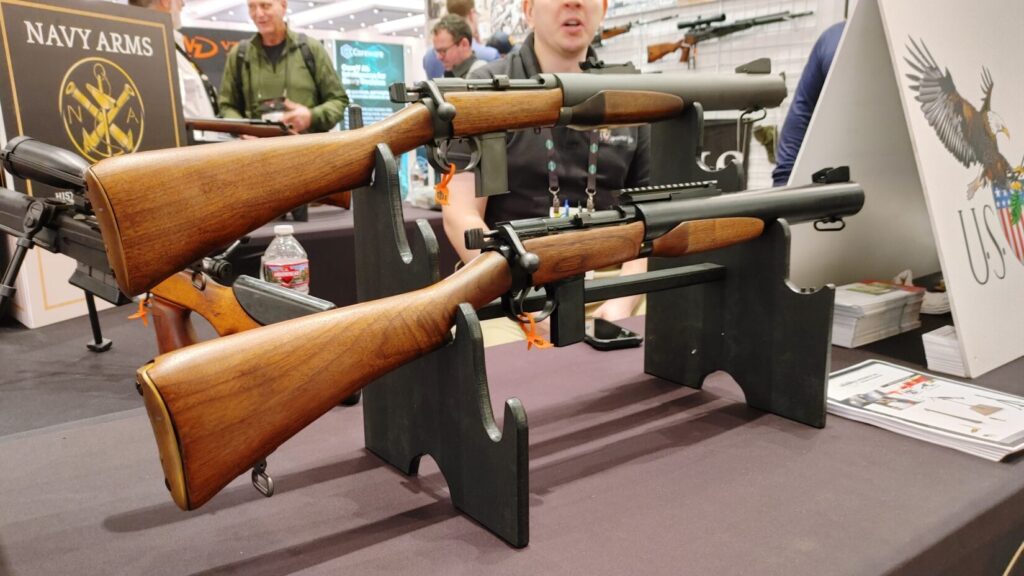 A bolt-action De Lisle carbine with an integrated suppressor and wooden stock displayed at a trade show.