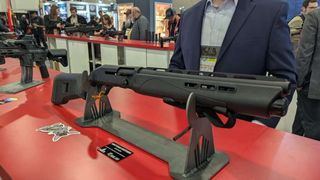 A modern semi-automatic tactical shotgun with a Magpul stock and M-LOK handguard on a display stand at a trade show.