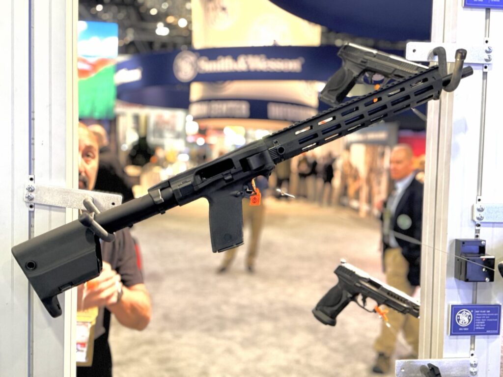 A Smith & Wesson FPC rifle displayed on a wall rack at a SHOT Show booth.