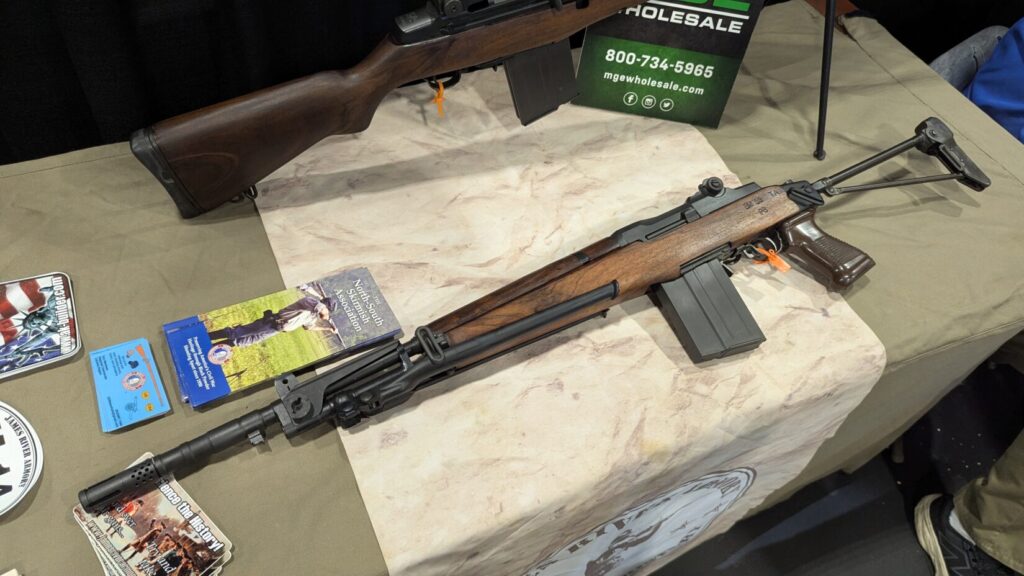 A Beretta BM59 paratrooper rifle with a folding stock and wooden handguard displayed on a table.