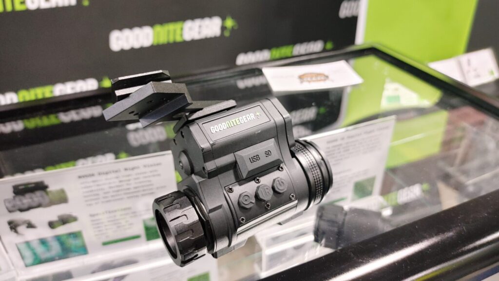 A Goodnitegear digital night vision device mounted on a bracket inside a glass display case.