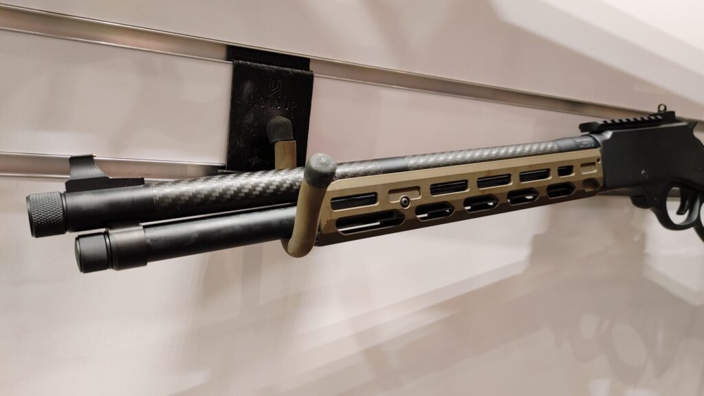 A modern lever-action rifle with an olive drab stock and an M-LOK handguard mounted on a display wall.