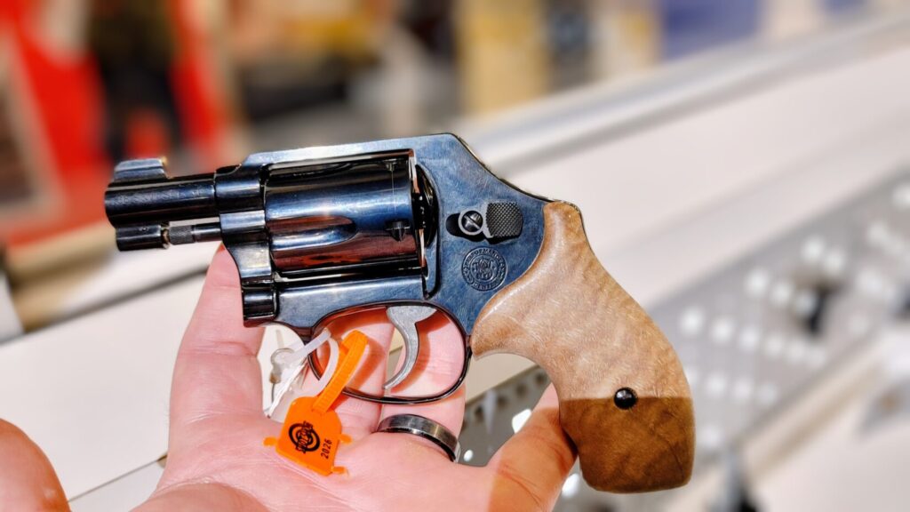 Small black revolver with smooth wooden grips held in a person's hand.