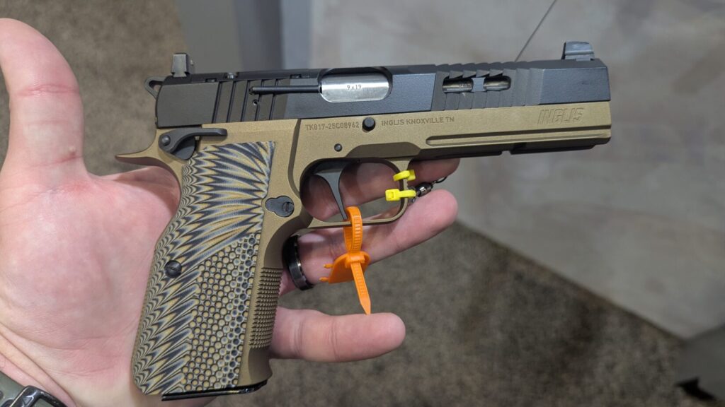 An Inglis Hi-Power with a tan frame, black slide, and textured G10 grips held by a attendee.
