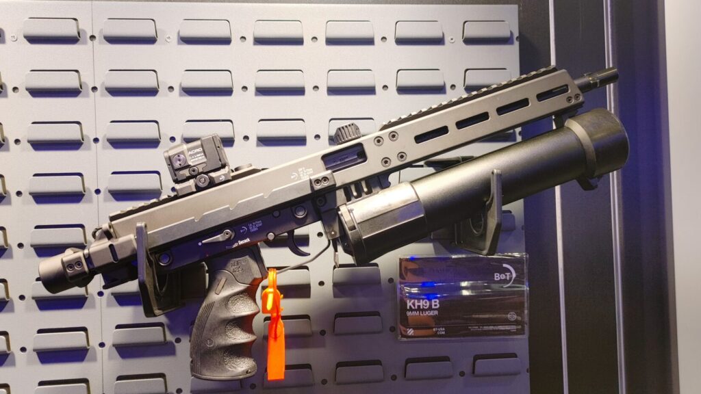 The B&T KH9 B mounted on a display wall, showing its Sites-inspired receiver and large cylindrical magazine.  