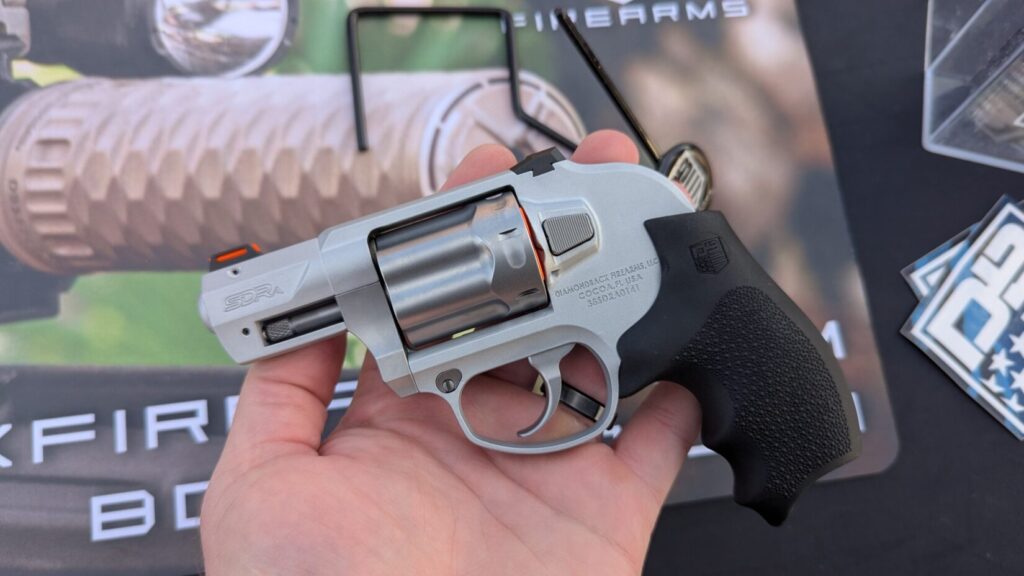 The left side of a silver .38 SPL +P revolver held in a hand against a background featuring the Diamondback Firearms logo.