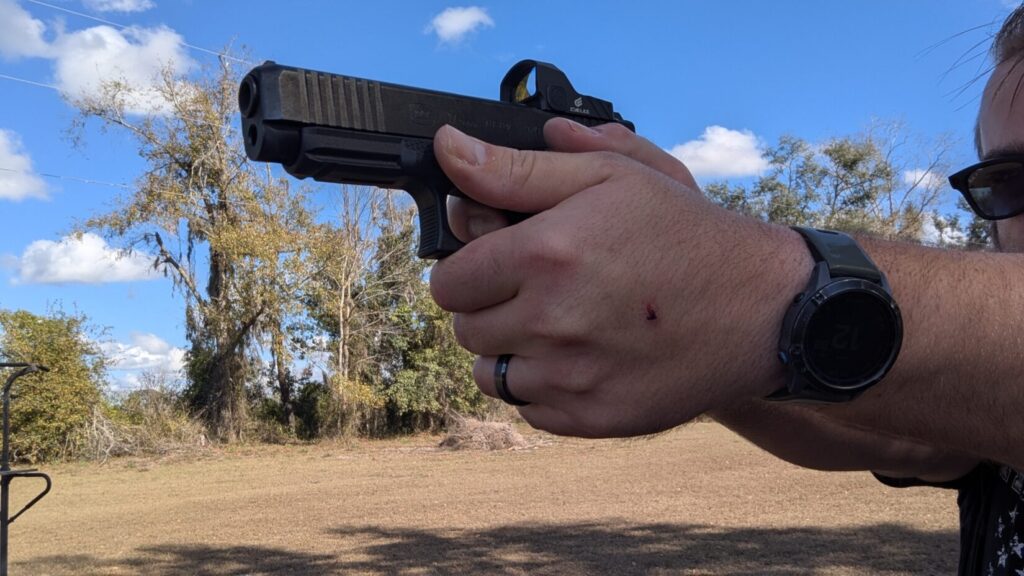 A close-up side view of a person's hands maintaining a firm, two-handed grip on a black Glock 17 pistol equipped with a red dot sight.