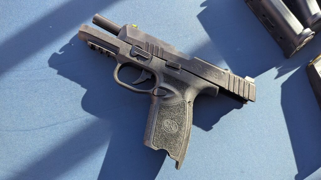 A black FN 509 semi-automatic pistol with the slide locked back, resting on a blue surface.