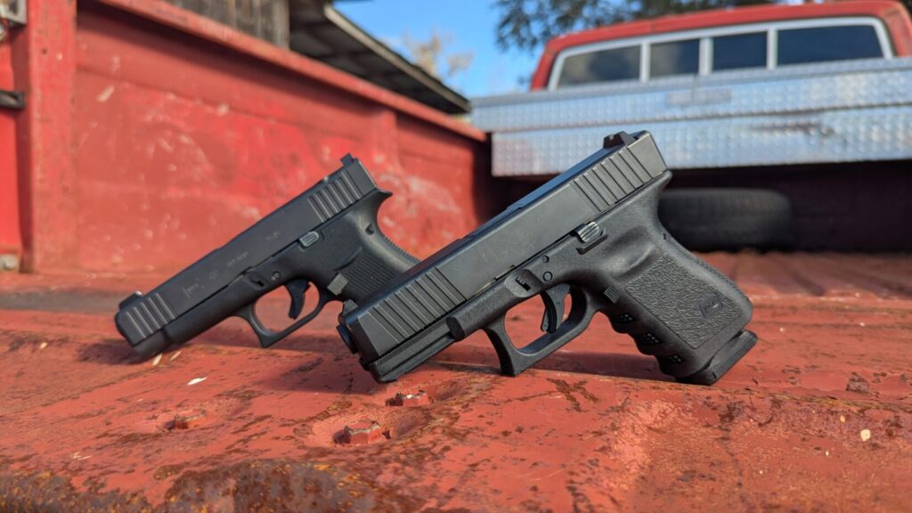 Two black pistols positioned diagonally on a rusty red surface with a pickup truck in the background.