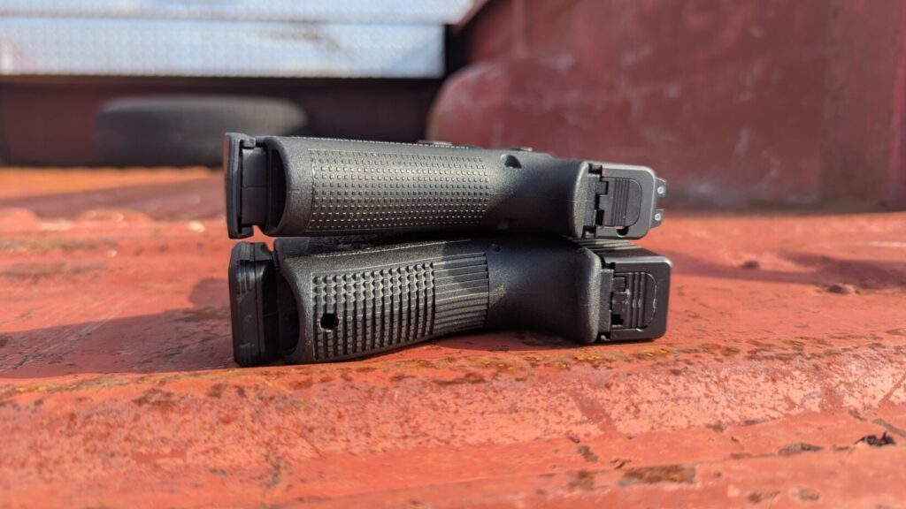 Close-up comparison of the grip thicknesses of two stacked black pistols, highlighting the difference between a slim and standard frame.