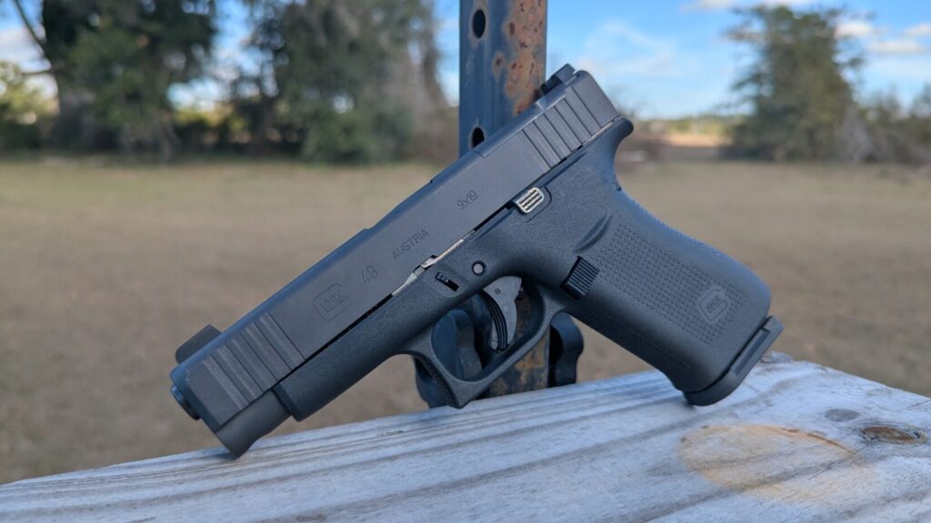 Side profile of a Glock 48 9mm pistol resting against a metal post outdoors.