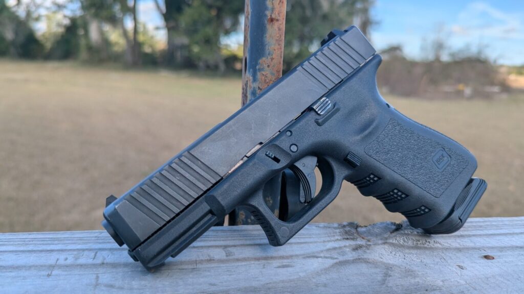 Close-up side view of a black Glock pistol with front slide serrations resting on a wooden ledge.