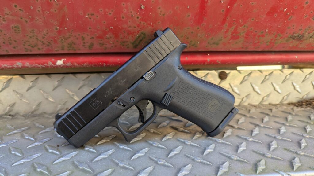 A Glock 43X pistol resting on a diamond-plate metal step next to a red vehicle.